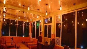 A room with wooden furniture, large windows, and hanging light fixtures. - Parker Camps (Baijnath)