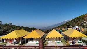 A row of yellow tents with a view of a mountainous landscape. - Parker Camps (Baijnath)