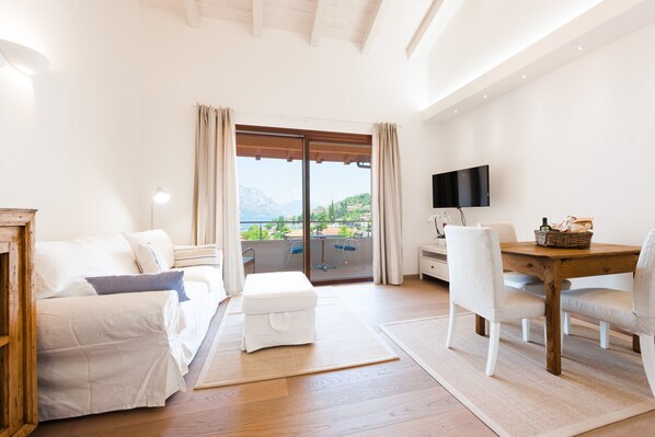 A modern living room with a balcony, white furniture, a flat-screen TV, and a wooden table. - Al vecchio frantoio in the center of town with beautiful lake views, near beach (Malcesine)