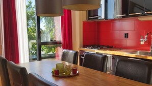 Et moderne spiseområde med et træbord og sorte læderstole, en rød accentvæg og et stort vindue med røde gardiner.