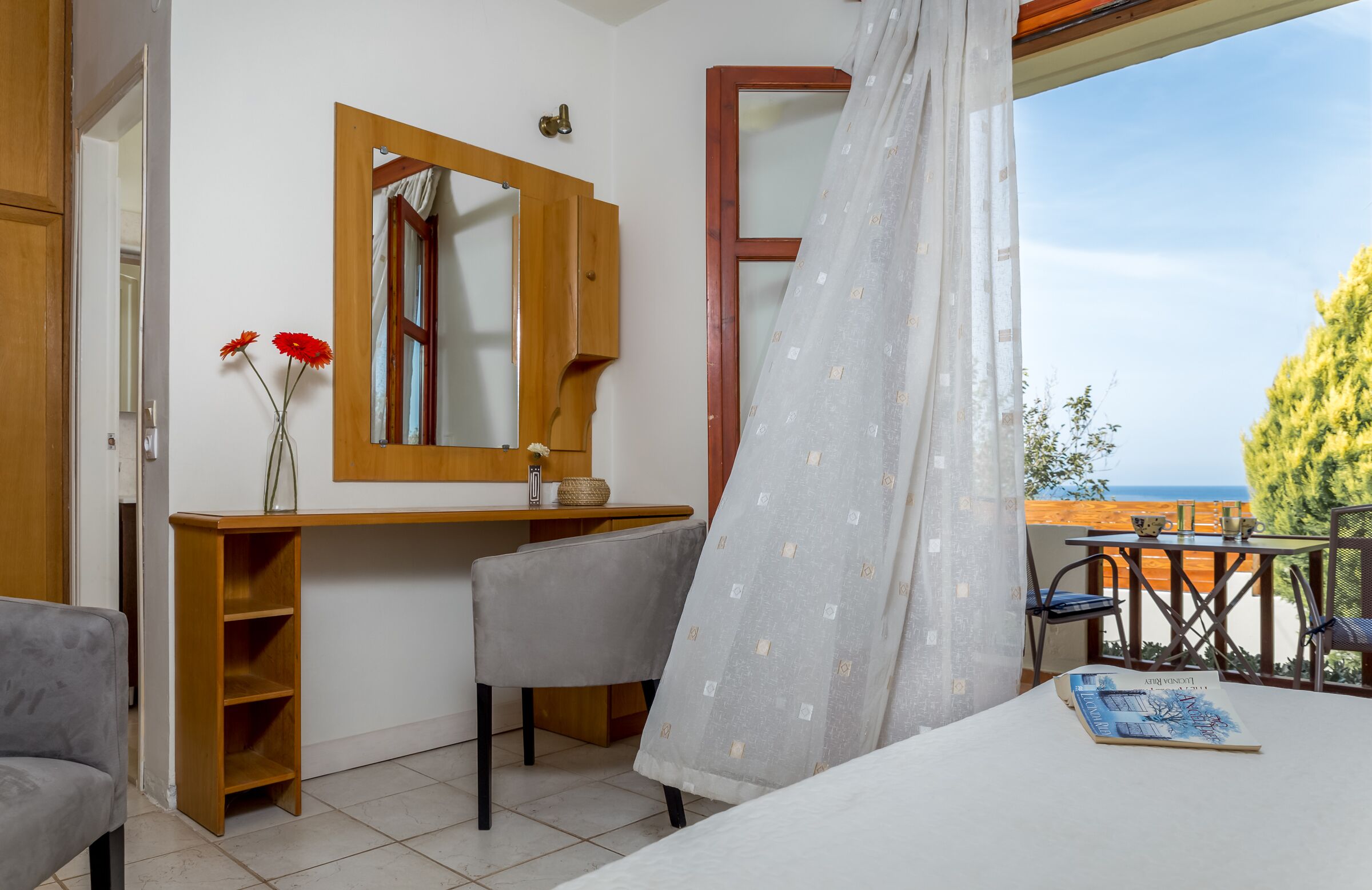 Una camera da letto con una scrivania in legno, una sedia, un comodino, uno specchio e vista sul mare.