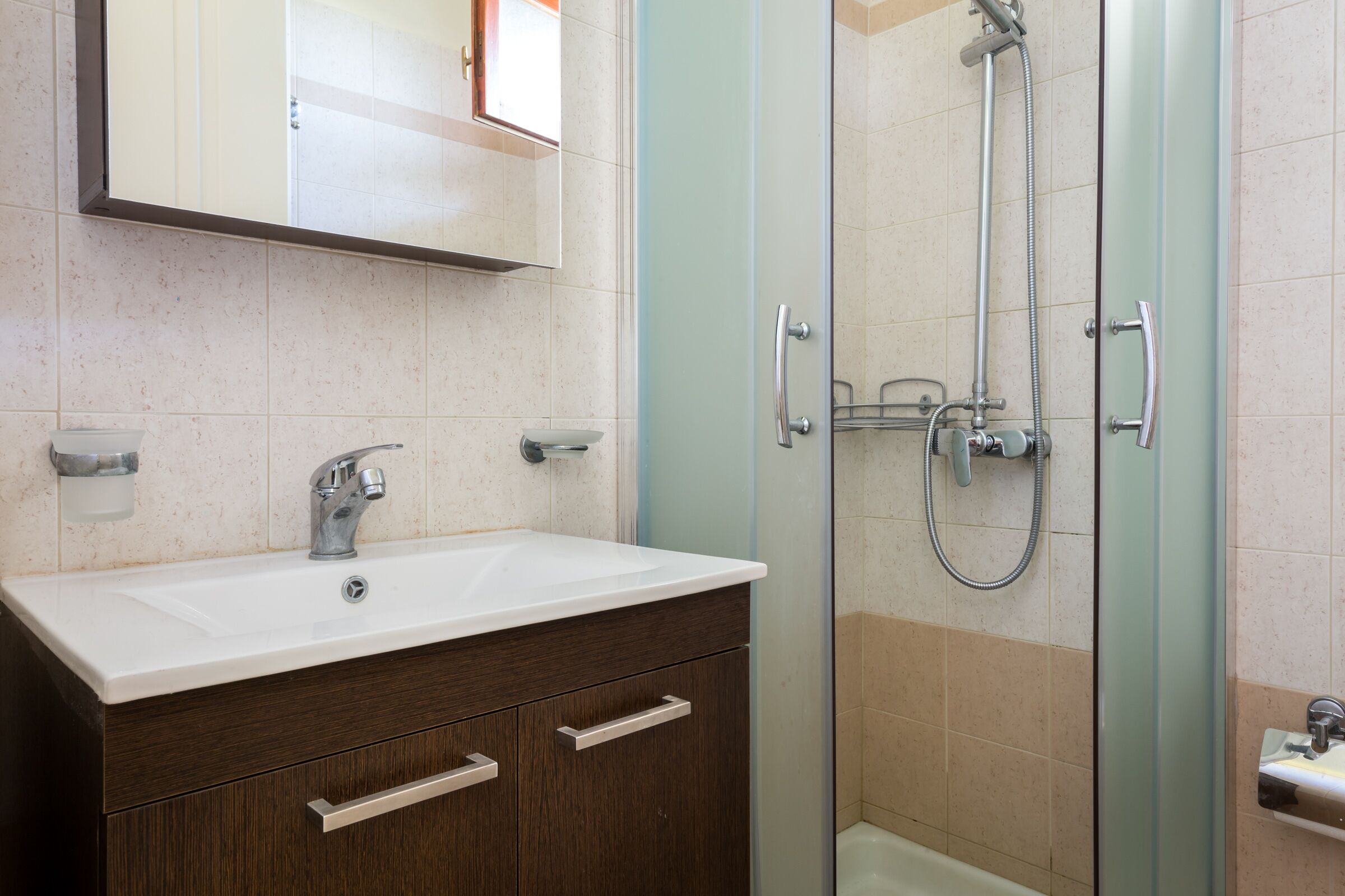 A bathroom with a white sink, dark wooden vanity, a glass shower enclosure, and a mirror above the sink.