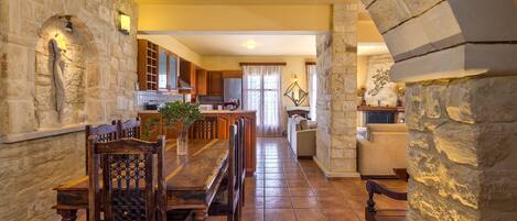 A spacious kitchen with stone walls, a dining area with wooden furniture, and a view into the living room.