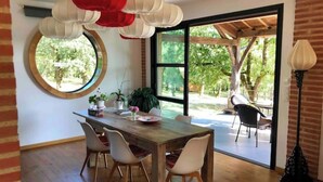 Un comedor con una mesa de madera, cuatro sillas, un espejo redondo y faroles rojos y blancos colgantes.