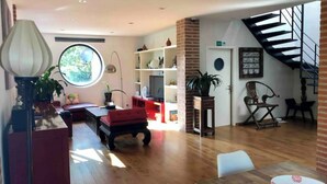 Un amplio salón con piso de madera, un sofá rojo, una mesa de comedor y una escalera que sube a un nivel superior.