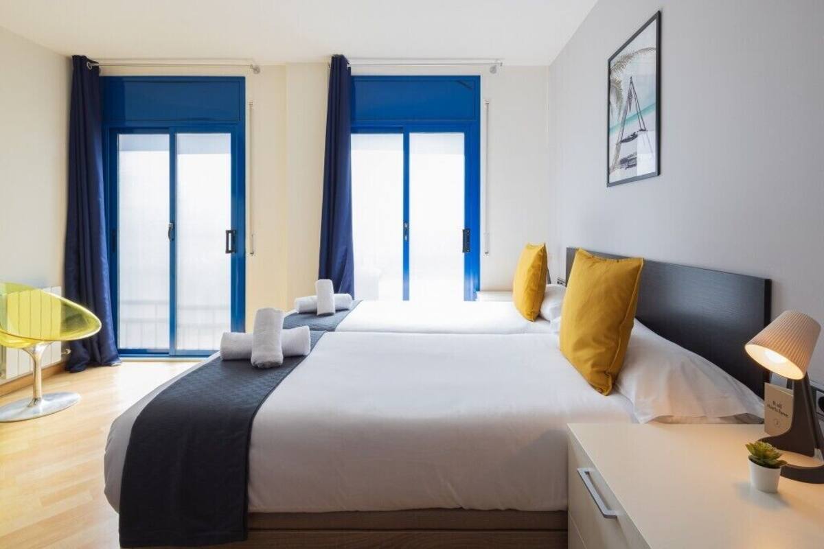 A hotel room with two beds, a desk, a chair, and a window with curtains.
