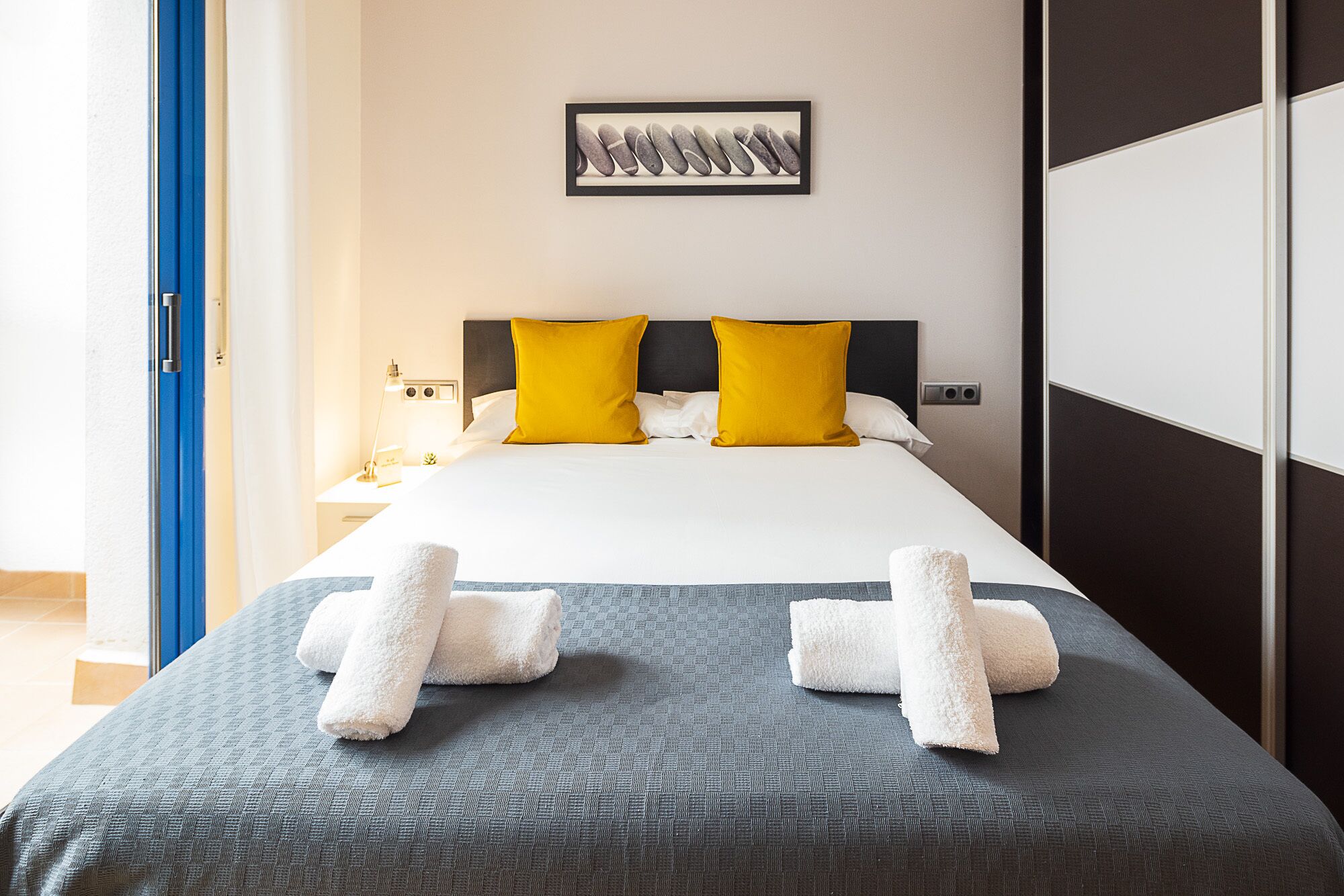 A hotel room with a bed, two pillows, a nightstand, a lamp, and a framed picture on the wall.