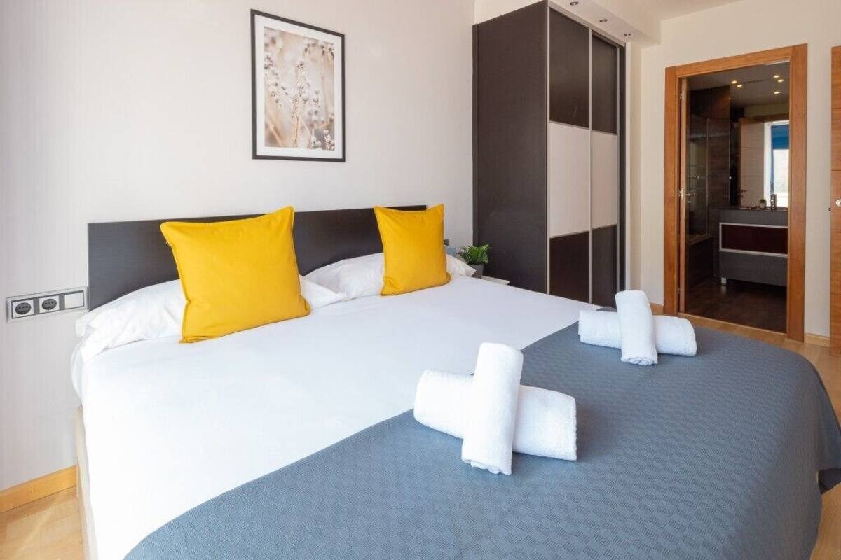 A hotel room with a large bed, two yellow pillows, a grey bedspread, and neatly folded white towels on the bed.