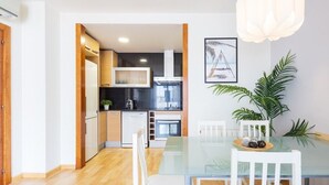 A modern kitchen with white cabinets, a black countertop, and a glass dining table with white chairs. - Lucas House by Sitges Group (Sitges)