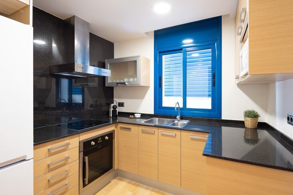 Eine moderne Küche mit schwarzen Arbeitsplatten, Holzschränken, einem eingebauten Ofen und einem Fenster mit blauen Fensterläden.