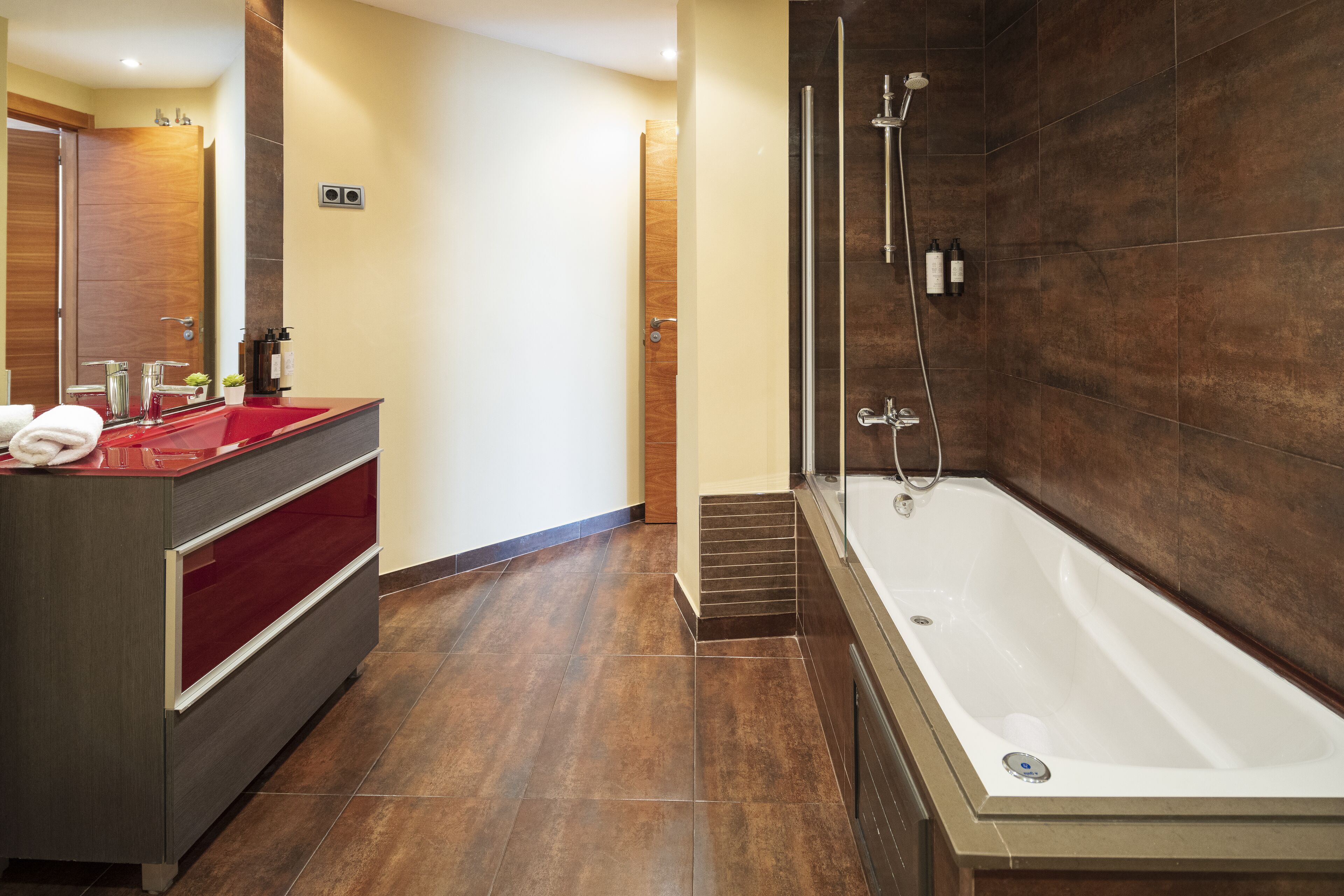 Un bagno moderno con una vasca da bagno grande, un mobile bagno rosso e una porta in legno.
