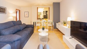 A modern living room with a grey sofa, a TV, a dining area with white chairs, and a kitchen in the background. - Lucas House by Sitges Group (Sitges)