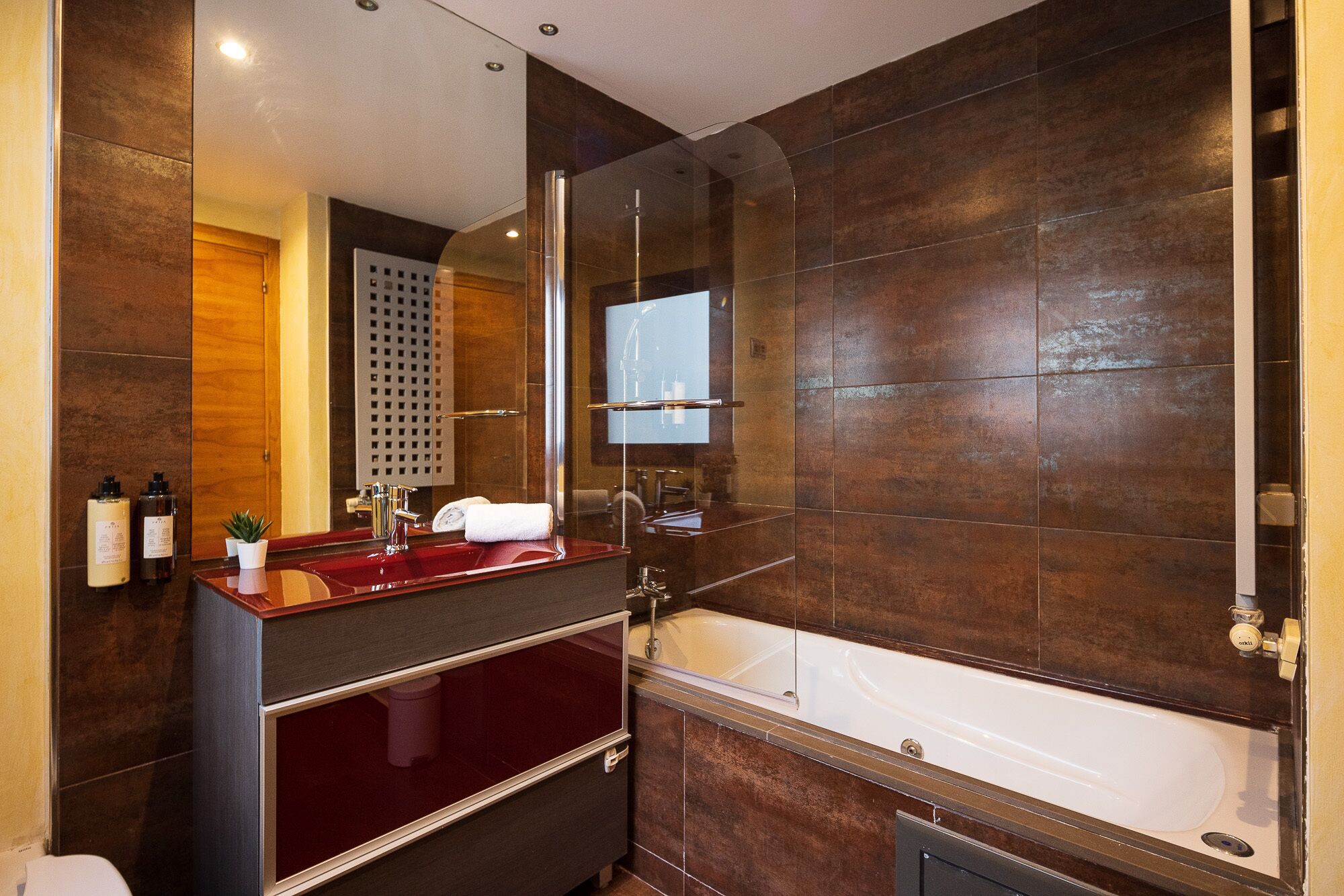 A modern bathroom with a large mirror, a bathtub, and a vanity with a red countertop.