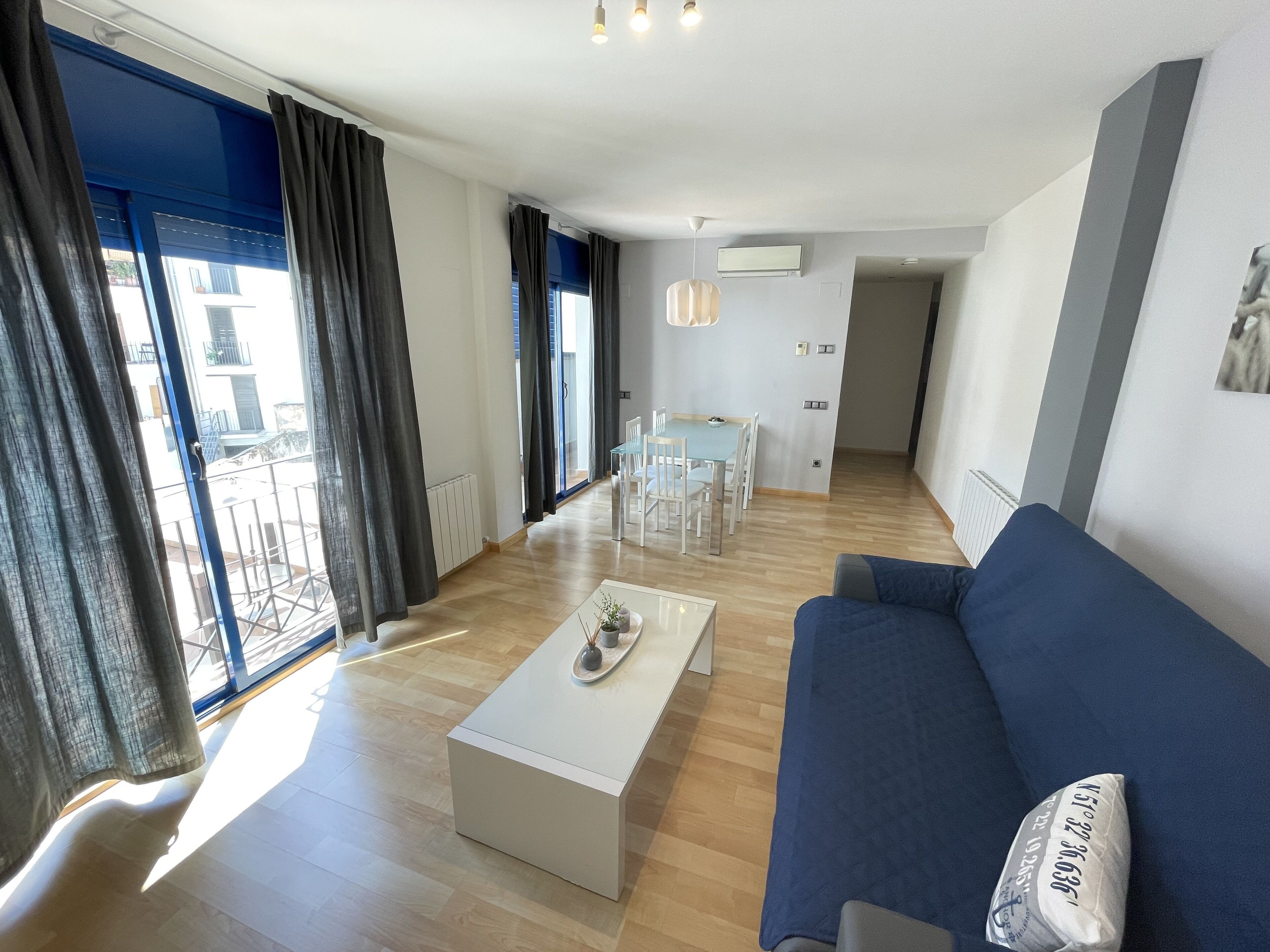 A modern living room with a blue sofa, a white coffee table, and a dining area with chairs and a table.