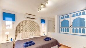 A hotel room with a large bed, a headboard with a geometric pattern, a wall with blue architectural designs, a window with a view, and a nightstand with a lamp. - 'Villa Tiphareth' with Private Pool, Wi-Fi and Air Conditioning (Marbella)