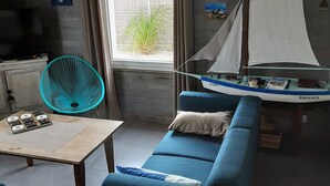 Ett vardagsrum med en blå soffa, ett litet bord, en fläkt och en modell av en segelbåt.