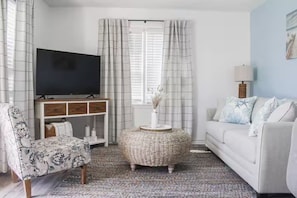 Een woonkamer met een televisie op een dressoir, een bank, een fauteuil en een decoratieve mand.