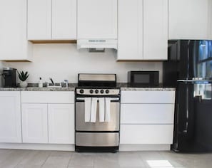 A modern kitchen with white cabinets, a stainless steel oven with towels, a black refrigerator, and a microwave. - Near Ocean l Steps from Beach l Full Kitchen (Myrtle Beach)
