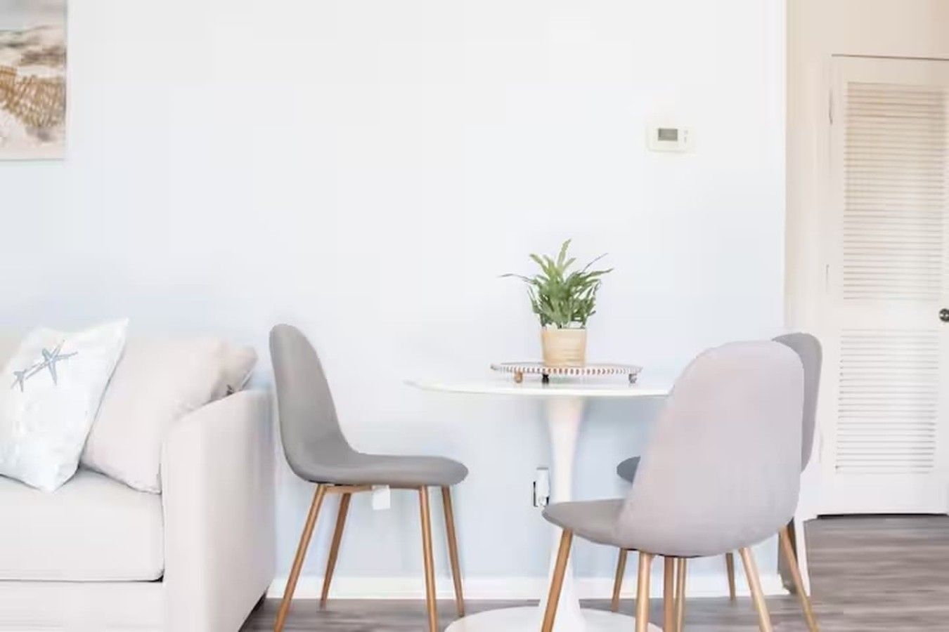 A modern living room with a white sofa, two grey chairs, a small round table with a plant, and a white door with louvered panels.