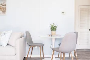 A modern living room with a white sofa, two grey chairs, a small round table with a plant, and a white door with louvered panels. - Near Ocean l Steps from Beach l Full Kitchen (Myrtle Beach)