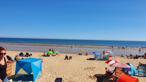 Una playa con tiendas de campaña, sombrillas y gente.