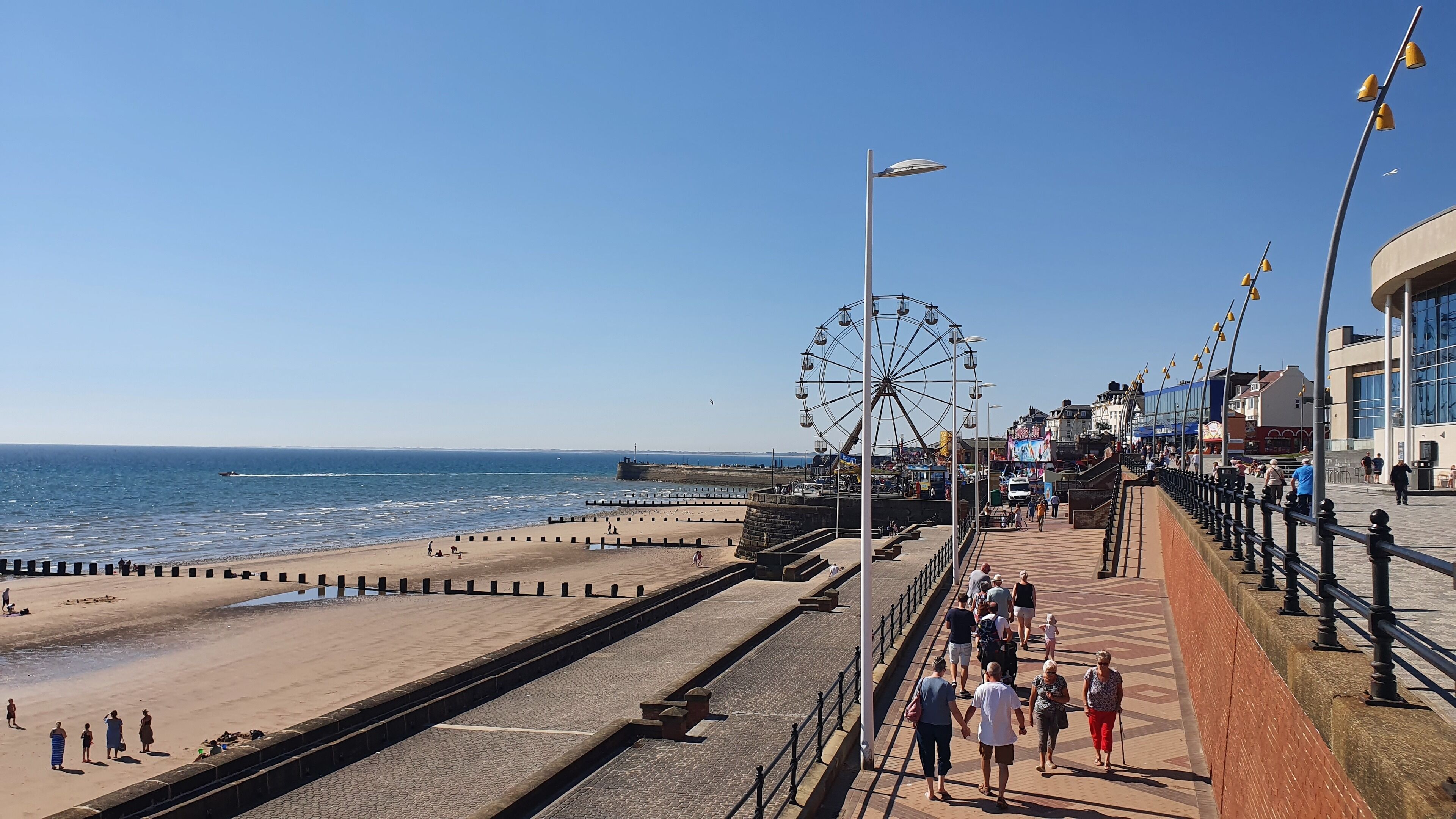 Eine Uferpromenade mit Riesenrad, Strand und Häuserzeile.