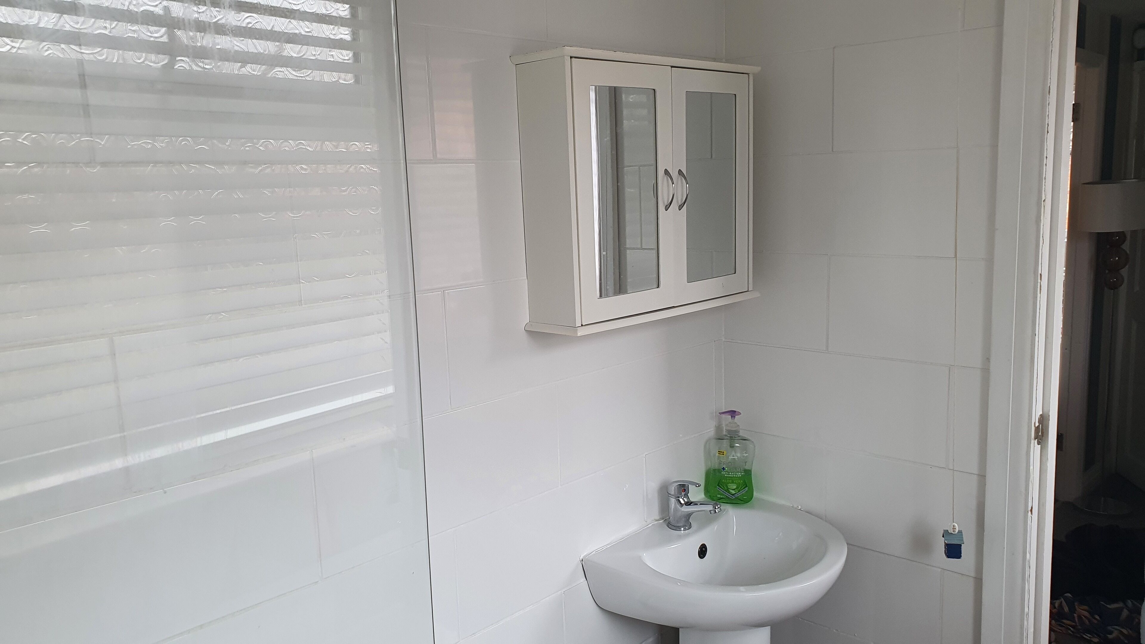 Une salle de bain avec un lavabo blanc, un meuble vitré et une fenêtre avec des stores.