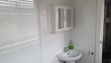 Une salle de bain avec un lavabo blanc, un meuble vitré et une fenêtre avec des stores.