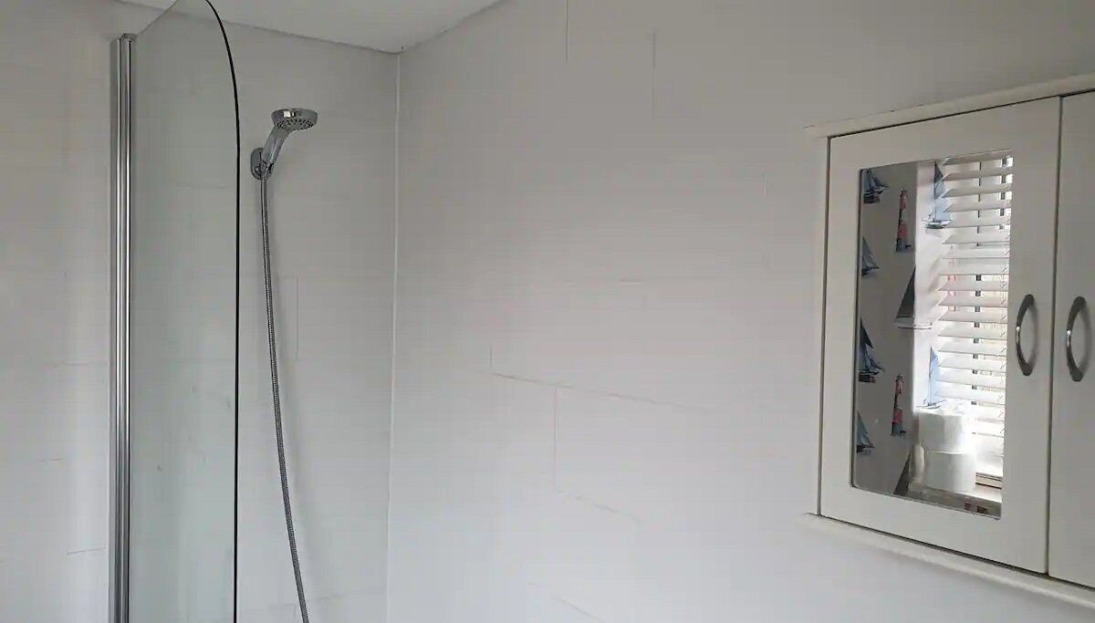 A bathroom with a shower, a mirror cabinet, and a white tiled wall.