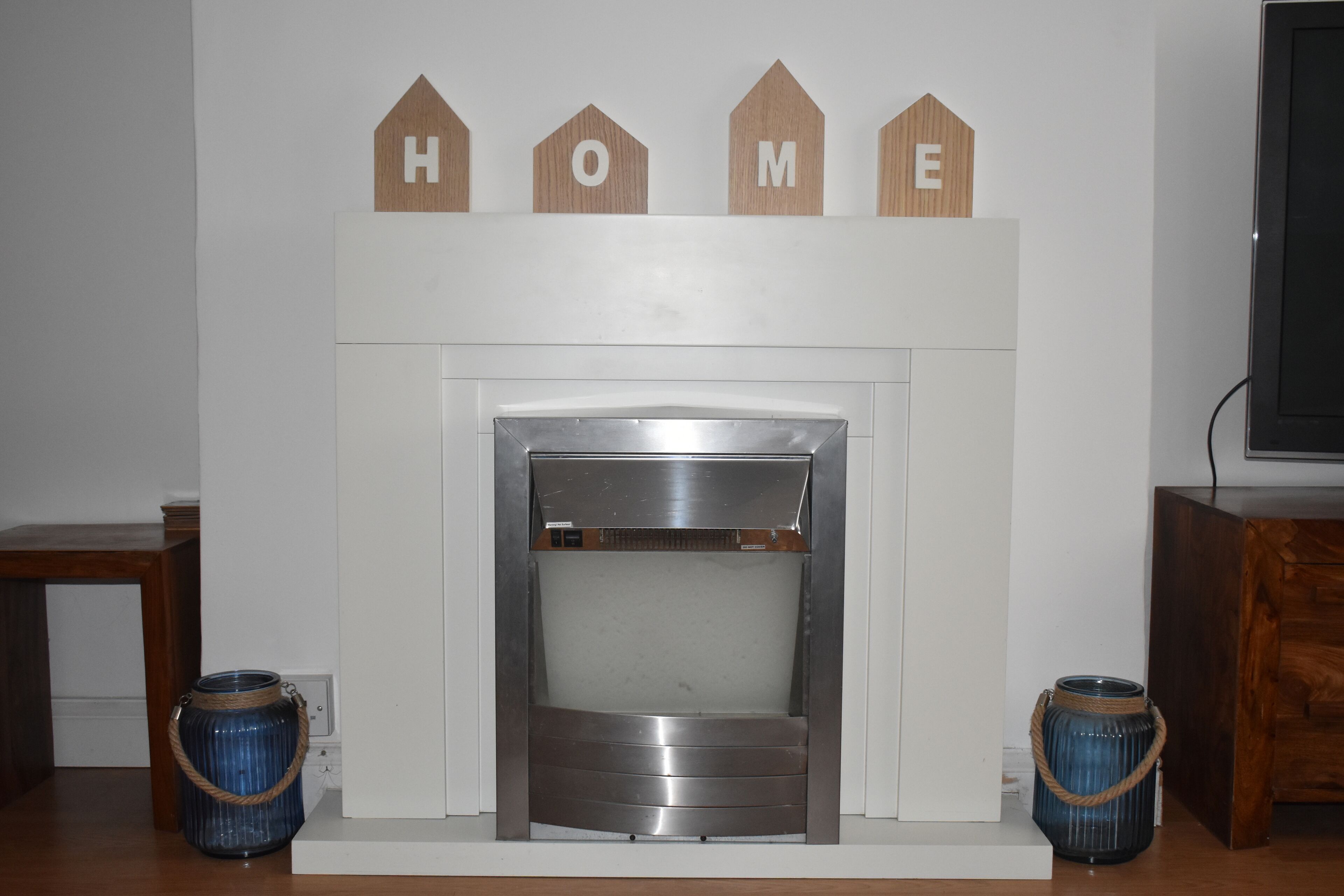 Una chimenea de diseño moderno, flanqueada por dos jarrones decorativos. Sobre la chimenea, letras de madera que dicen 
