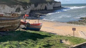 A coastal scene with two boats on a sandy beach, cliffs in the background, and a clear sky. - Cedar Boutique Lodge-dog, Fishing and Spa Access (York)