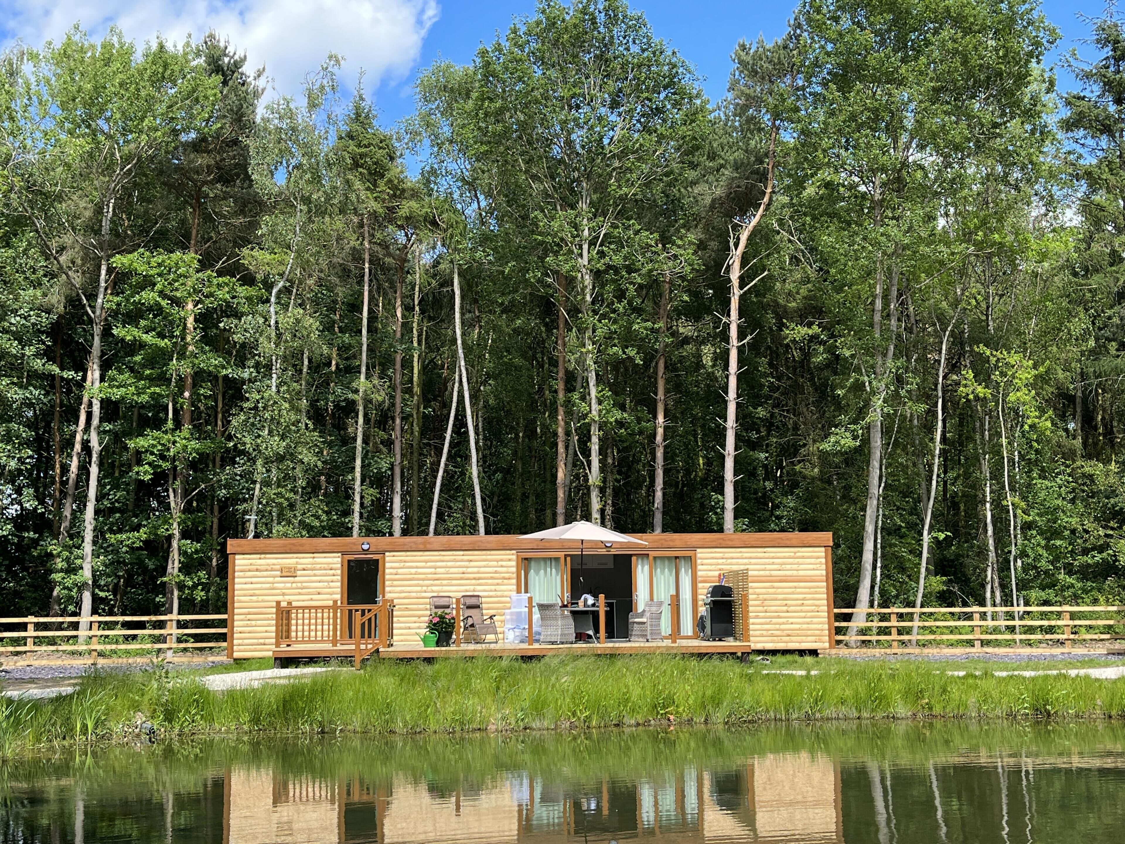 A wooden cabin with a deck, a small porch, and a window overlooking a pond.