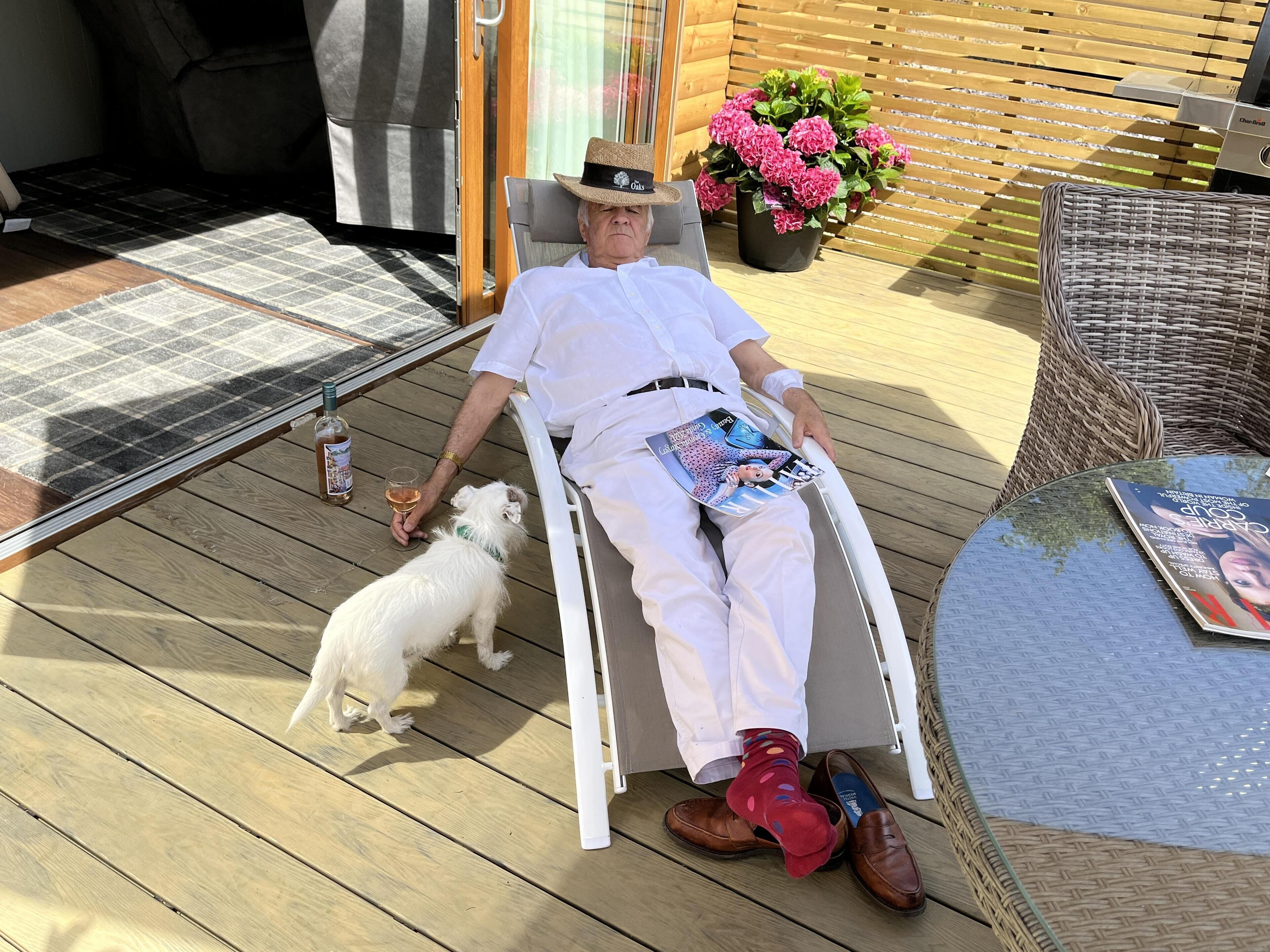 A person in a wheelchair on a wooden deck with a dog, a magazine, and a bottle of alcohol.
