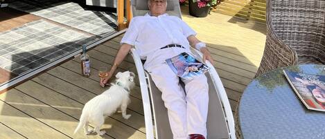 A person in a wheelchair on a wooden deck with a dog, a magazine, and a bottle of alcohol.