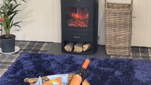 A room with a wood-burning stove, a potted plant, a wicker basket, and a blue rug. - Cedar Boutique Lodge-dog, Fishing and Spa Access (York)