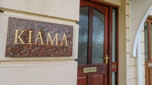 Une plaque de numéro de maison portant le nom « KIAMA », fixée sur un mur à texture.