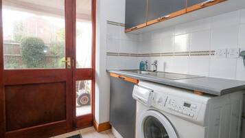 A compact kitchen with a built-in washing machine, a sink, and a door leading to a balcony.