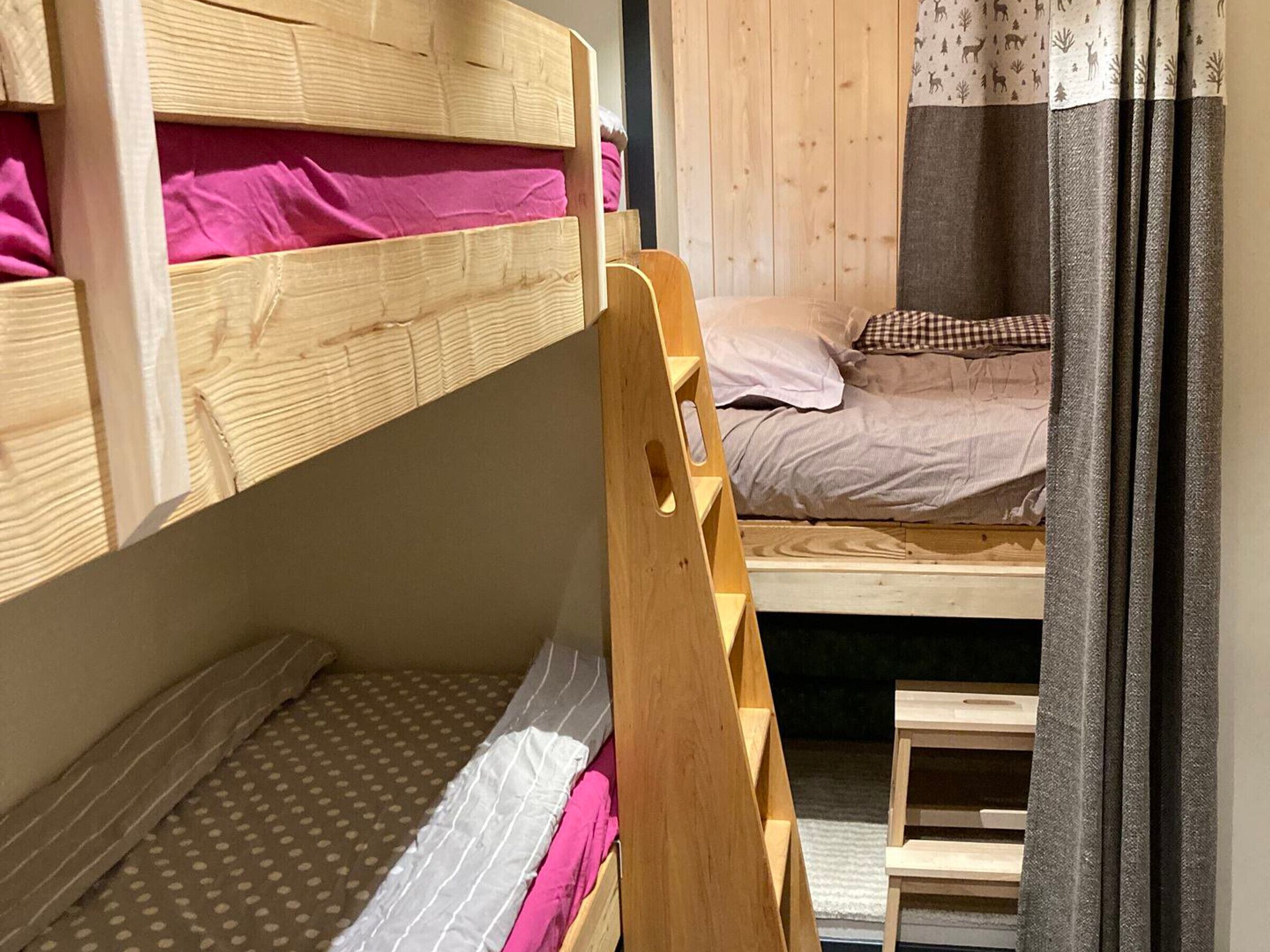 Quarto com beliche, uma escada de madeira, um banquinho pequeno e cortina com padrão de veado.