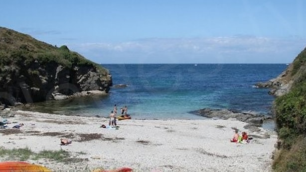 A beach with rocky cliffs, clear blue water, and people relaxing on the sand.