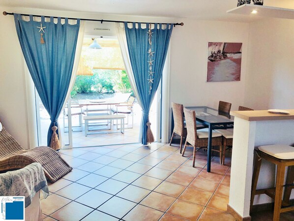 Una habitación con zona de comedor, sofá y ventana con cortinas azules.