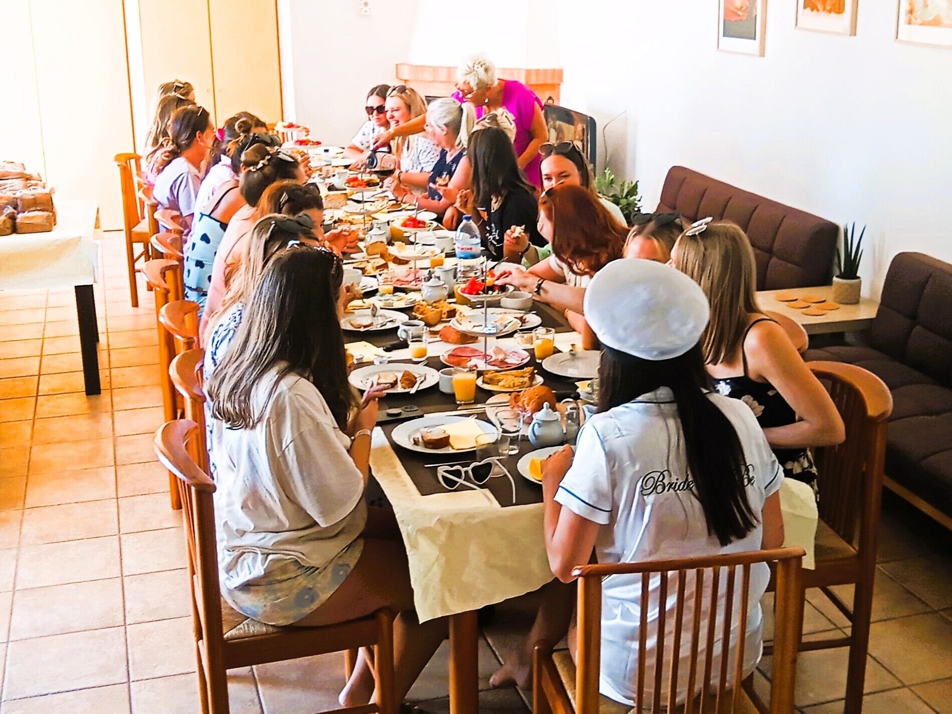 Un grupo de personas sentadas alrededor de una mesa larga en una habitación con sillas de madera y piso de baldosas.