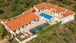 Una amplia villa con piscina, varias habitaciones para huéspedes y una cancha de tenis.