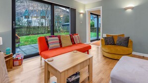 Un salon moderne doté d’une grande porte-fenêtre coulissante donnant sur un jardin, d’une table basse en bois et de deux canapés.