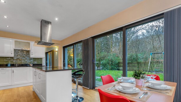 Une cuisine moderne avec des meubles blancs, un îlot central et un coin repas agrémenté de chaises rouges et d’une table dressée pour quatre personnes.