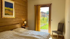 Een slaapkamer met een groot bed, een nachtkastje met een lamp, een stoel en uitzicht op een gebouw door een deur.