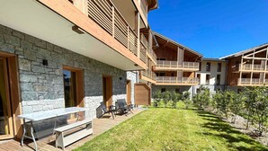 Een modern gebouw met een gevel van natuursteen, houten balkons en een gazon met terras.