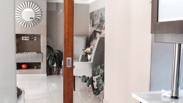 Un moderno vestíbulo de hotel con una puerta de madera que da a una zona de estar, un espejo grande y un mostrador de recepción.