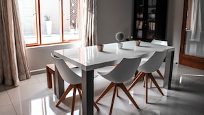 Un comedor moderno con una mesa y sillas blancas, una planta en maceta y una estantería.