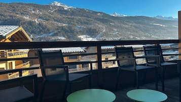 A balcony with two round tables and chairs, overlooking a mountainous landscape with buildings and a ski slope.