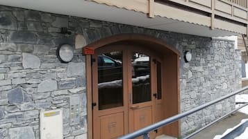 A stone building with a wooden door, a metal railing, and a snow-covered ground.